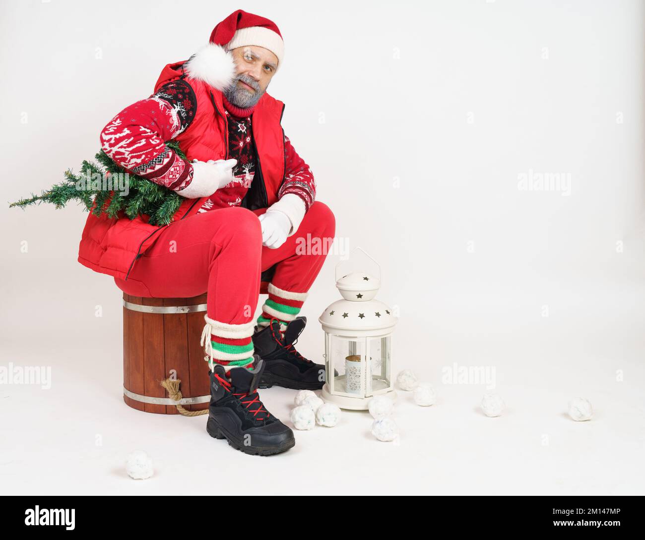 Holiday and Christmas concept. Santa Claus sits on a wooden bucket, holding a Christmas tree, next to a lantern. Stock Photo