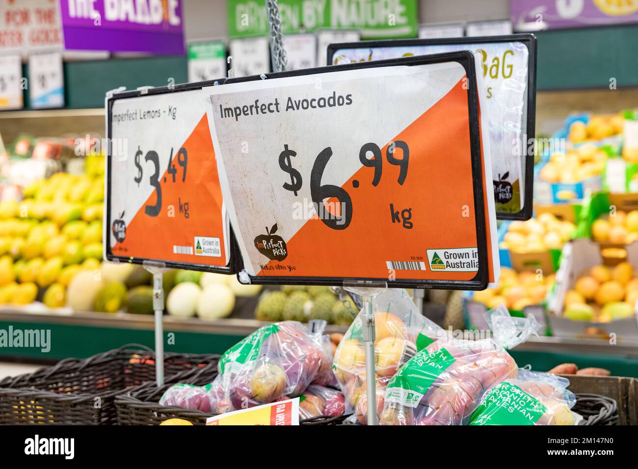 Imperfect avocados and imperfect lemons being sold in a Harris Farm supermarket in Sydney, price per kg displayed on the store sign, help reduce waste Stock Photo