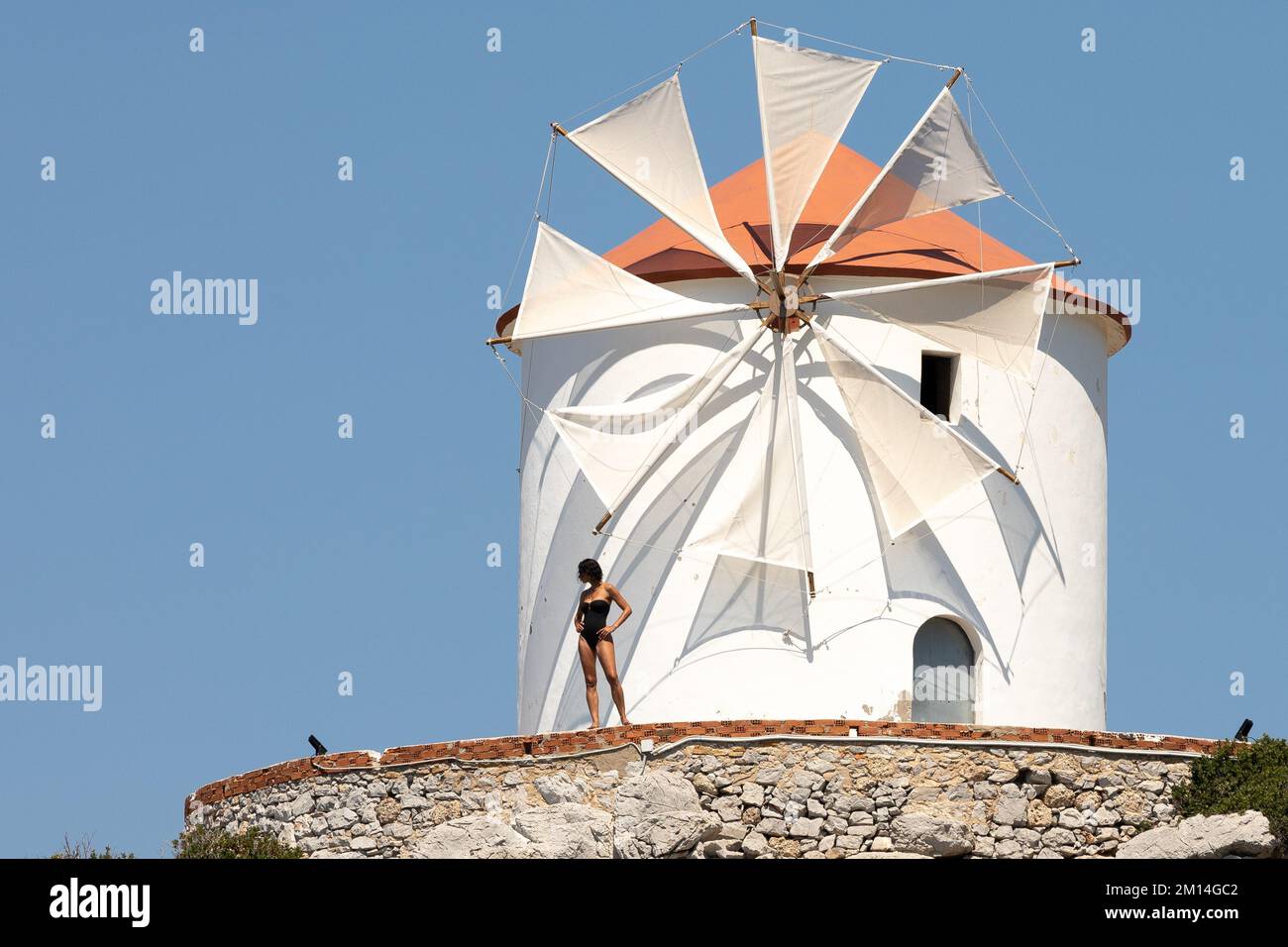 A woman in a black swimsuit standing in front of a windmill. Stock Photo