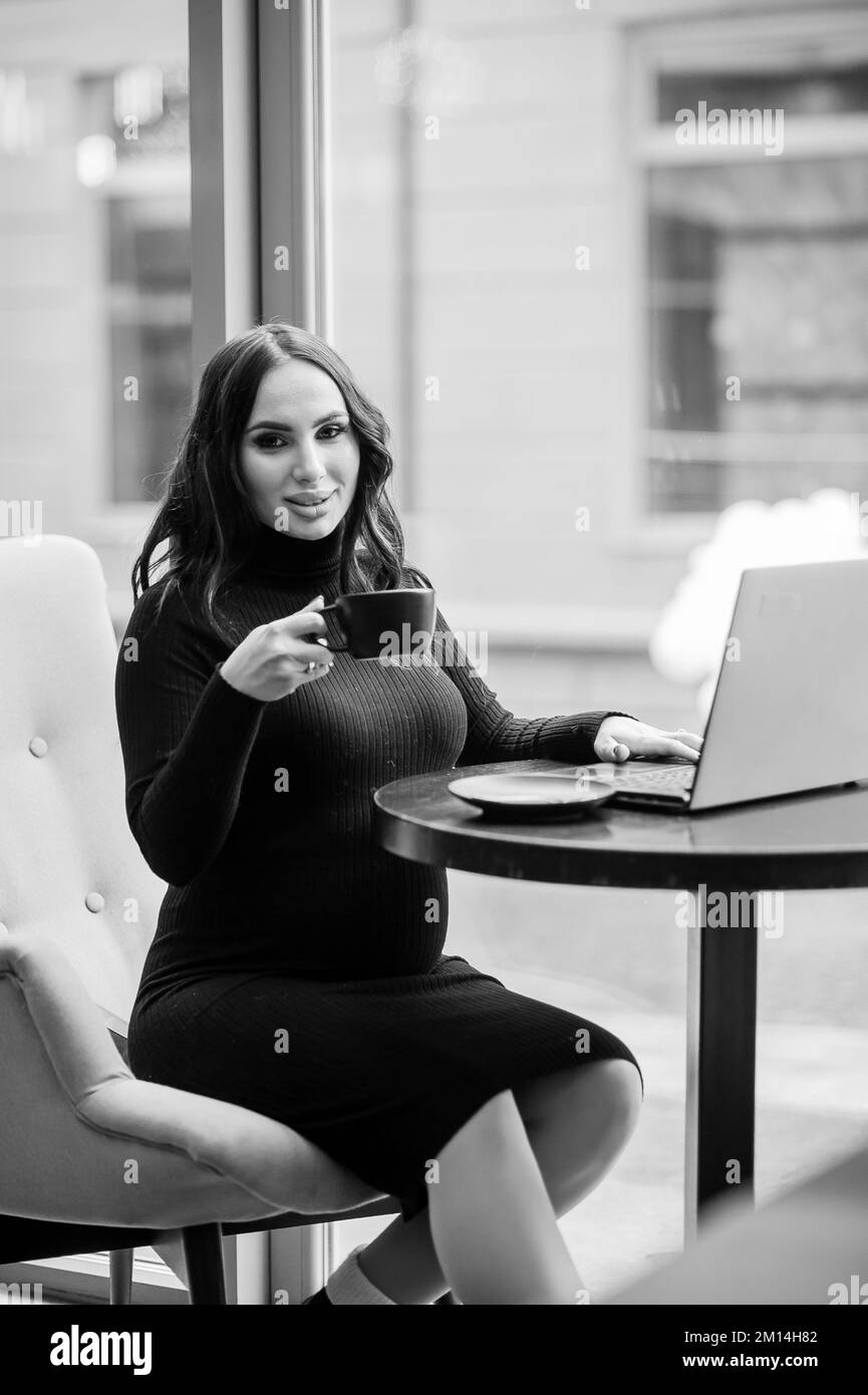 A pregnant business woman sits at a table in the office, works at a