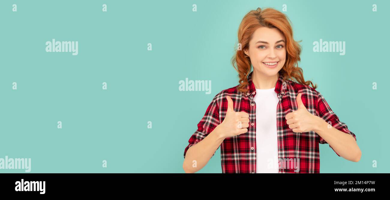 happy redhead girl in checkered shirt on blue background. thumb up. Woman isolated face portrait, banner with mock up copyspace. Stock Photo