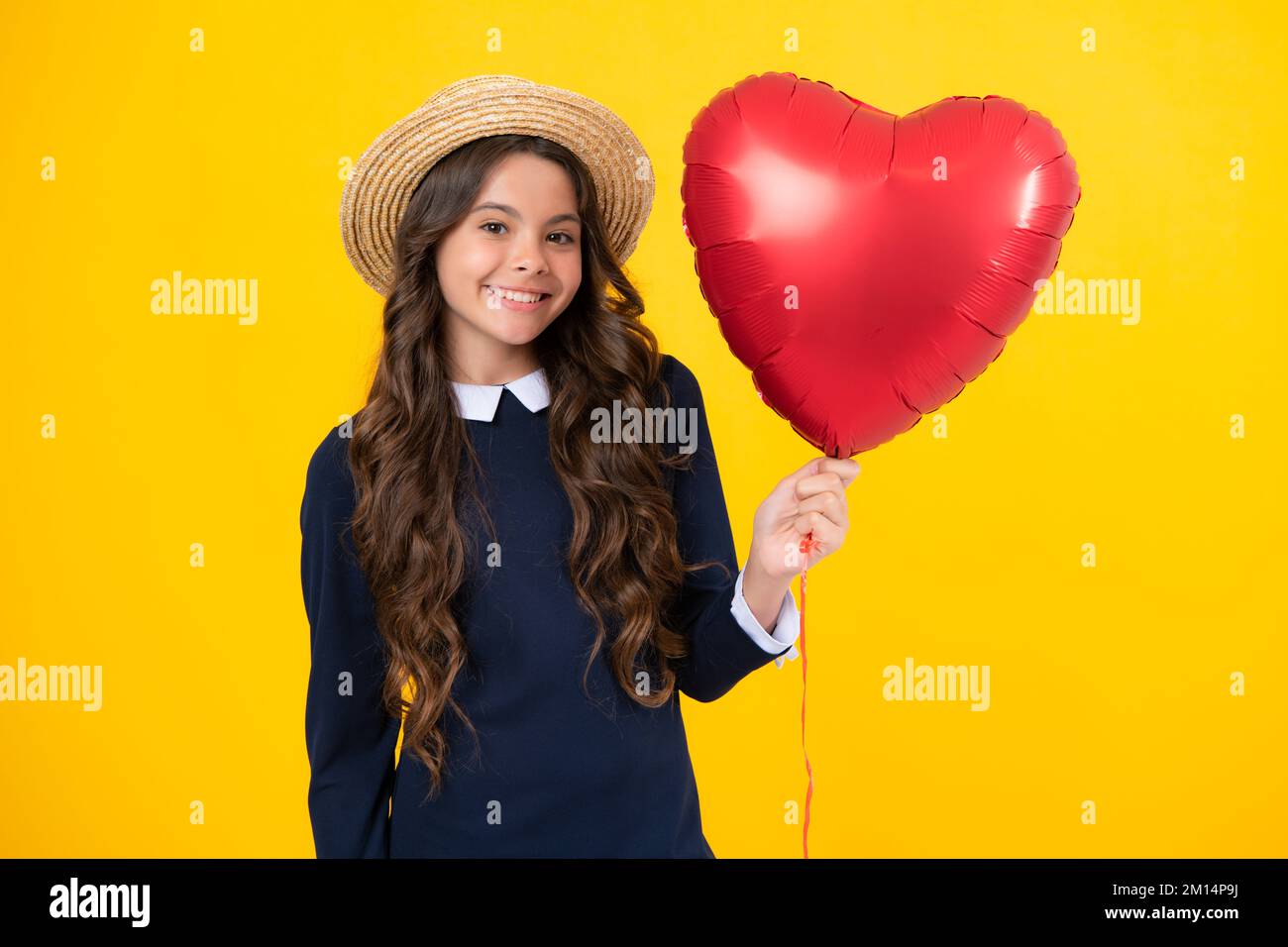 Lovely romantic teenage girl hold red heart balloon, symbol of love for valentines day isolated on yellow background. Stock Photo