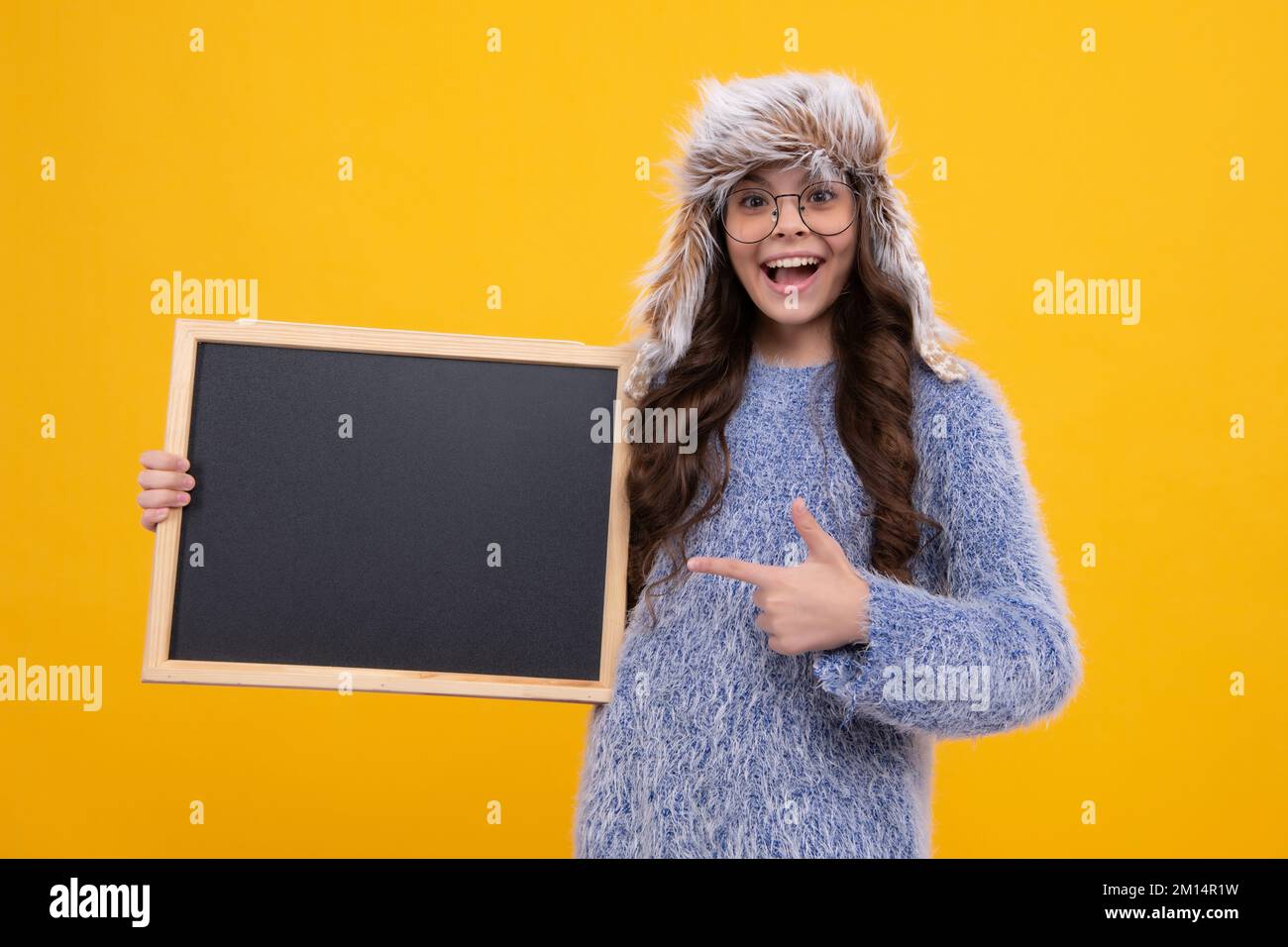 School sales board. Teen schoolgirl in warm winter hat hold blackboard. Back to school. Excited face, cheerful emotions of teenager girl. Stock Photo