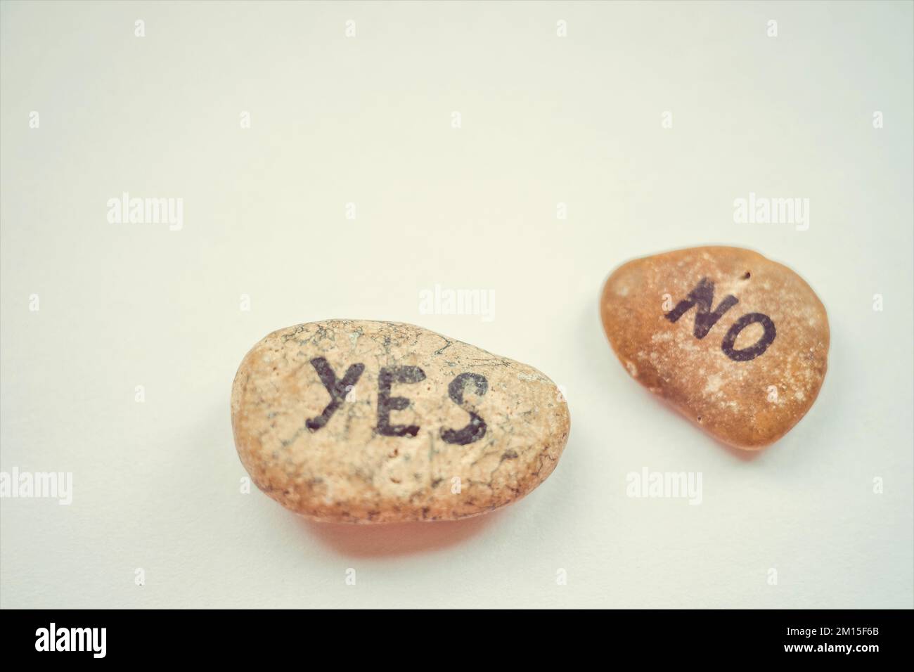 Two grey pebbles with the text yes and no on a blue table Stock Photo