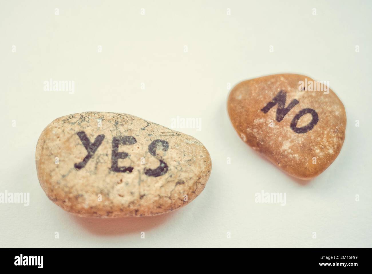 Two pebble stones with the text YES and NO on a beige table Stock Photo