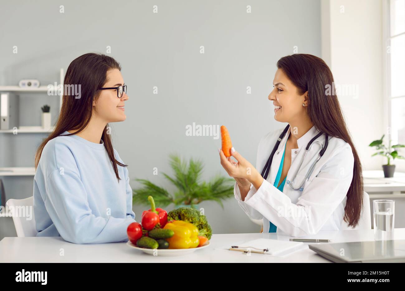 Young Caucasian woman sits at table with vegetables near doctor nutritionist in white coat Stock Photo