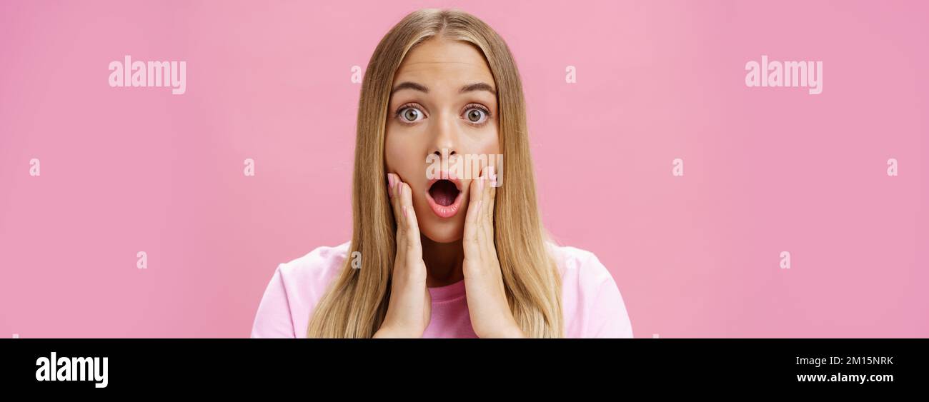 Close-up shot of shocked young female student with tanned skin and fair hair dropping jaw gasping from amazement touching cheeks surprised reacting to Stock Photo