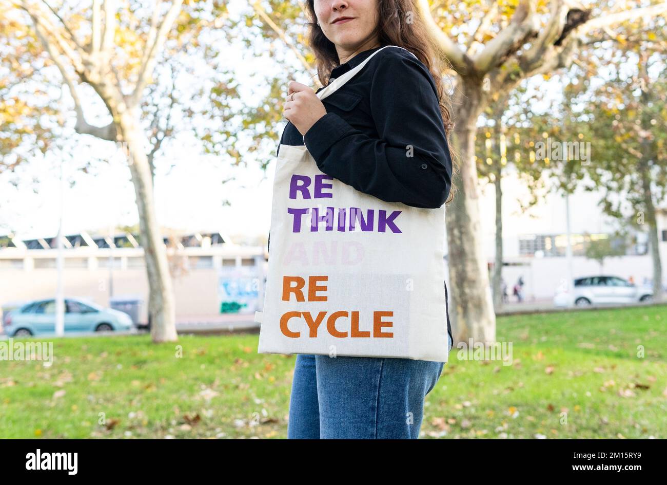 Side view of unrecognizable female in casual outfit holding bag with Rethink Recycle inscription while standing in summer green park Stock Photo