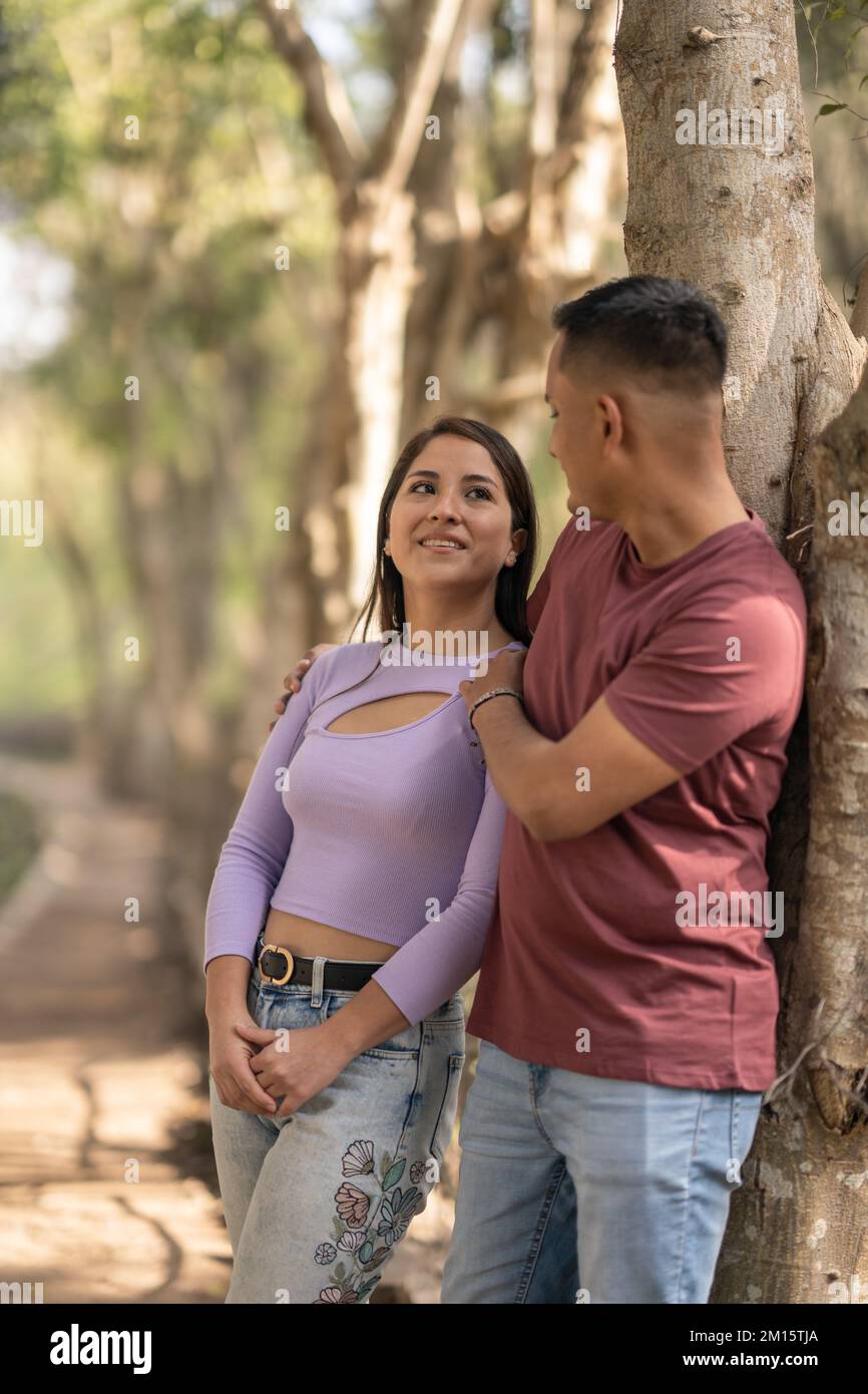 Side view of young man embracing woman from behind while leaning on ...