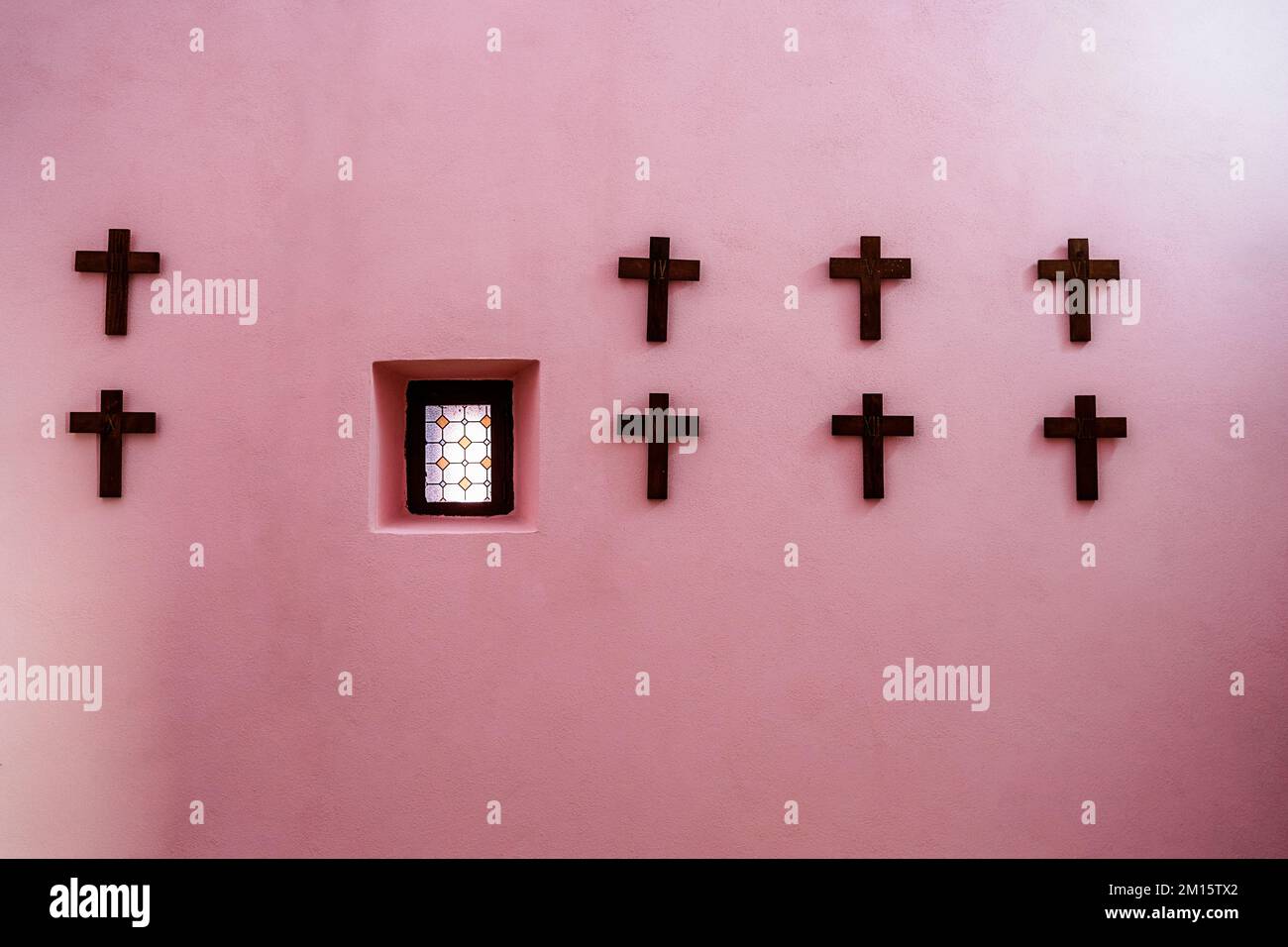 Black crosses hanging in rows on pink church wall near small stained