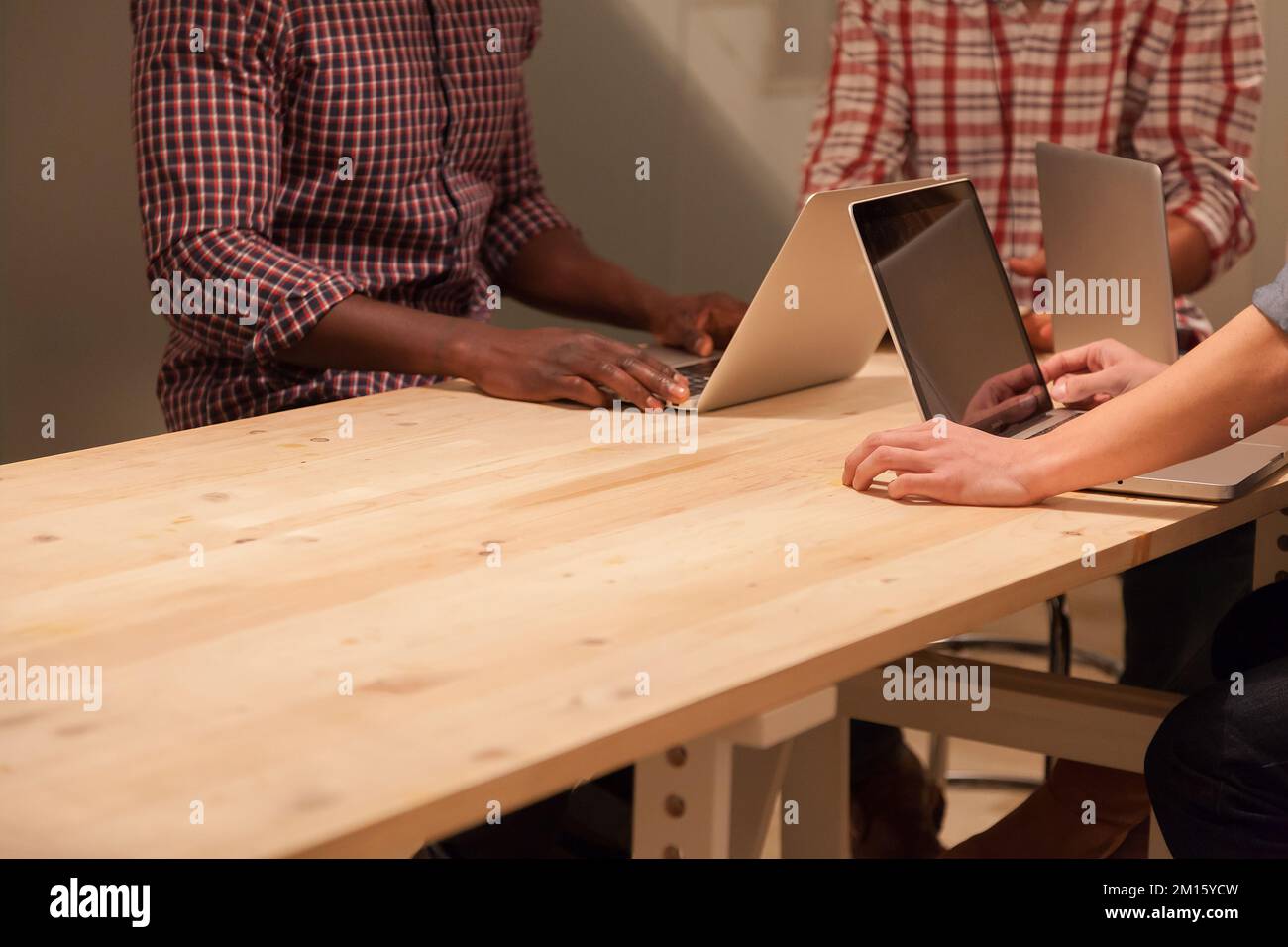 Three anonymous people Working on a Wooden Table with laptops Stock Photo