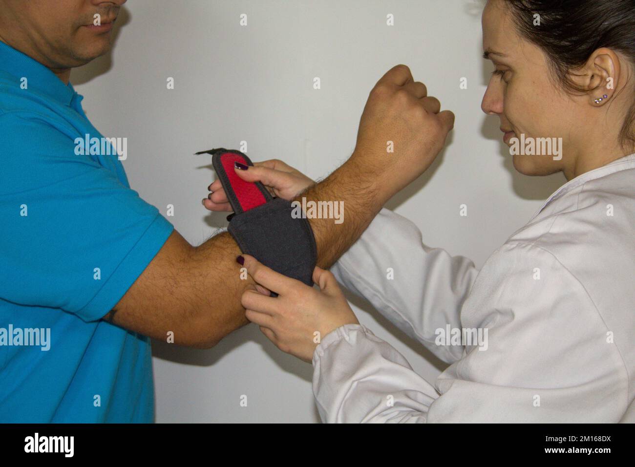 Image of a female physiotherapist showing a patient with epicondylitis pain how to put on the