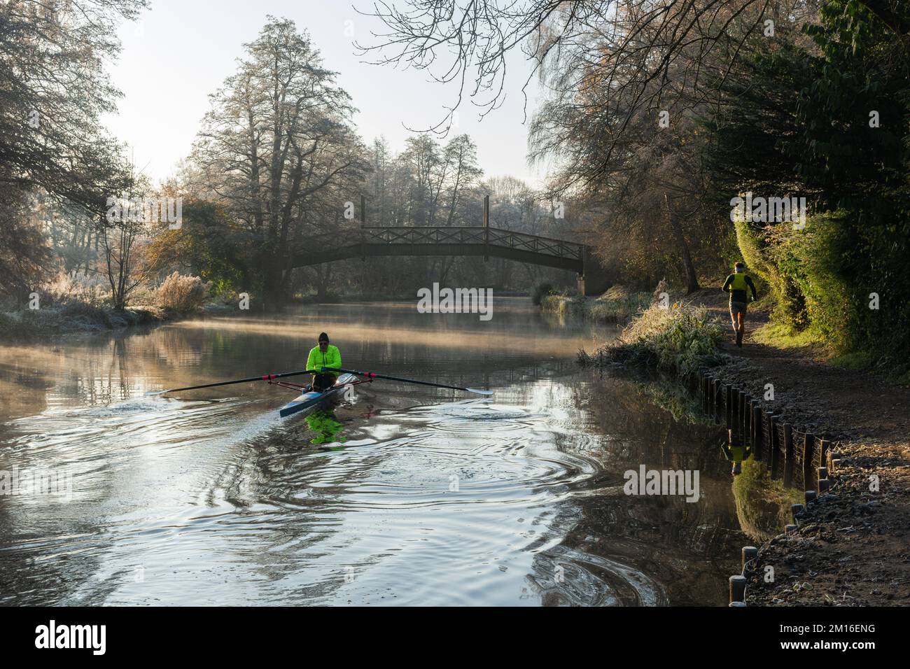 A single scull boat from Guildford Rowing Club on the River Wey on a cold frosty winter morning, Surrey, England, UK, and a jogger. 10th December 2022 Stock Photo