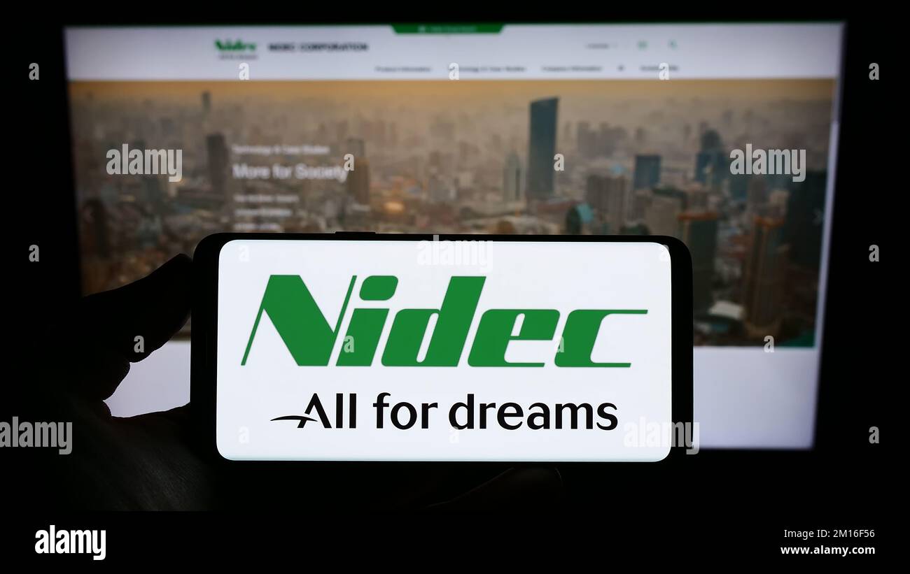 Person holding smartphone with logo of Japanese motor company Nidec Corporation on screen in front of website. Focus on phone display. Stock Photo