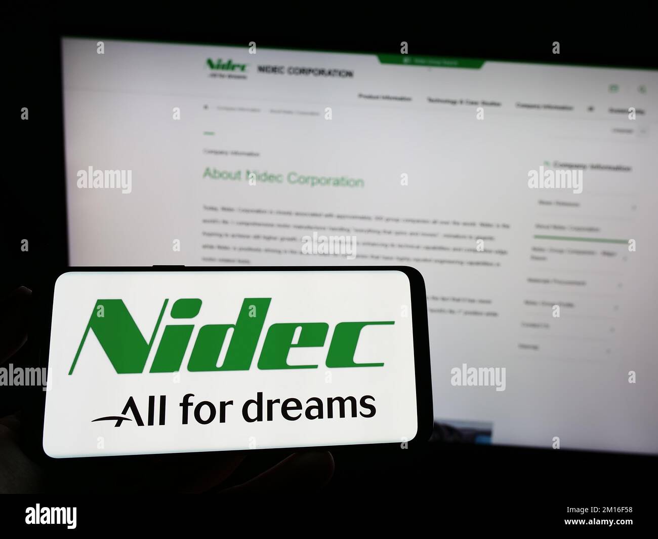 Person holding mobile phone with logo of Japanese motor company Nidec Corporation on screen in front of business web page. Focus on phone display. Stock Photo