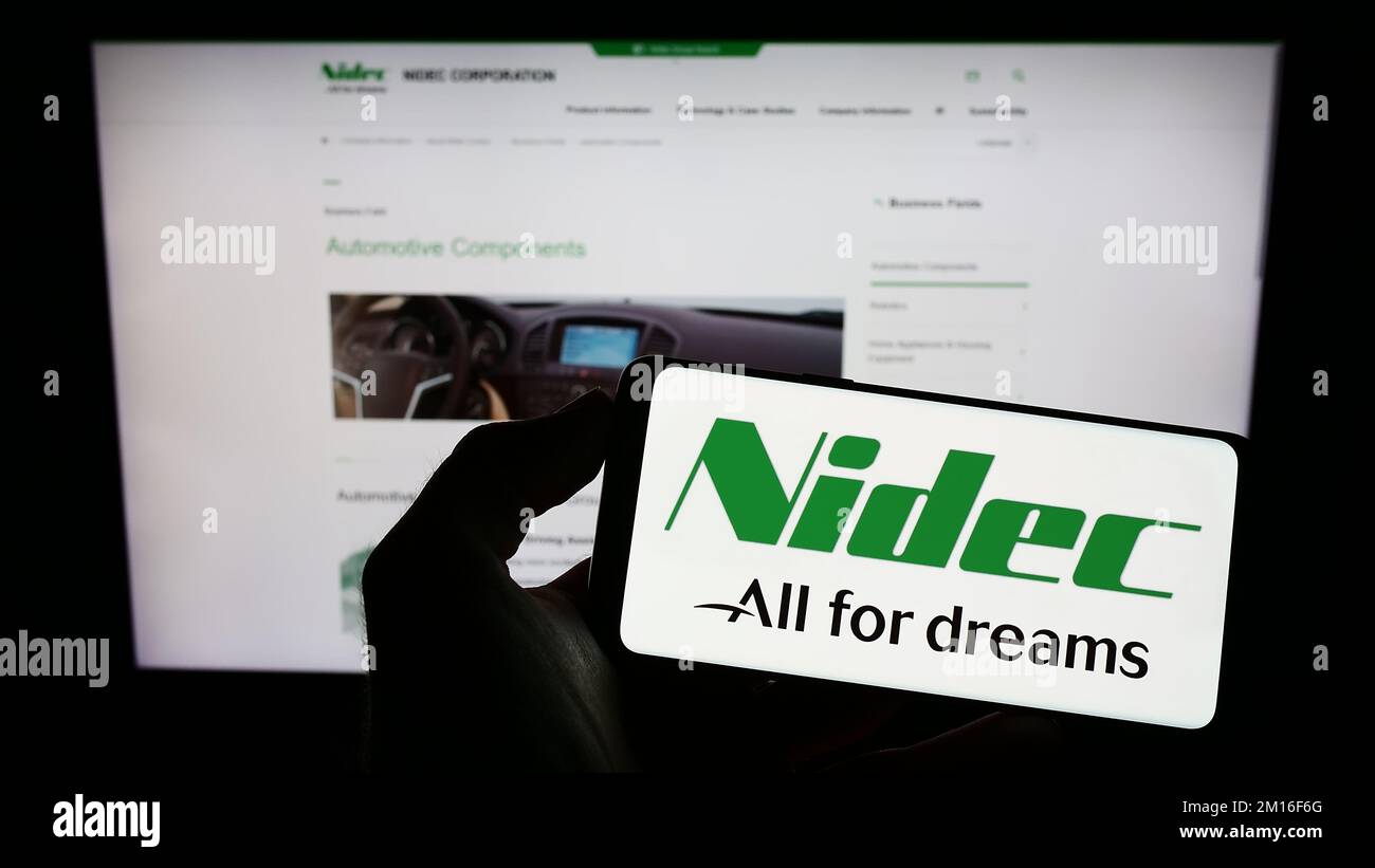 Person holding cellphone with logo of Japanese motor company Nidec Corporation on screen in front of business webpage. Focus on phone display. Stock Photo