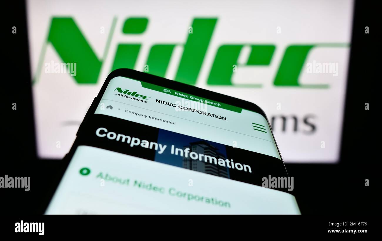 Mobile phone with webpage of Japanese motor company Nidec Corporation on screen in front of business logo. Focus on top-left of phone display. Stock Photo