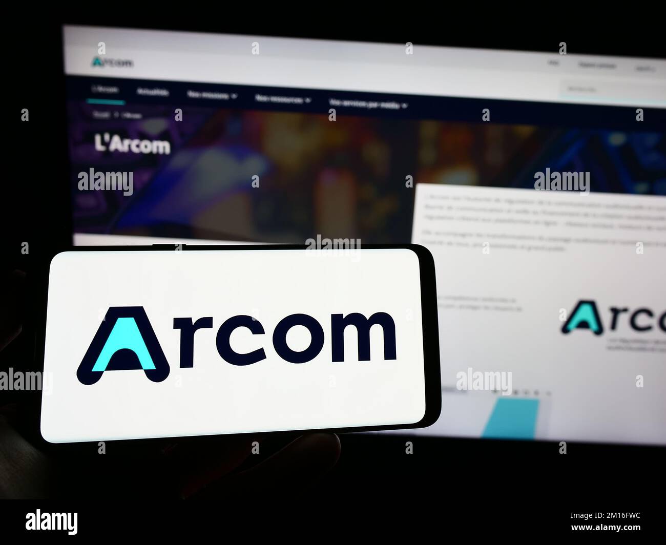 Person holding mobile phone with logo of French digital regulation agency ARCOM on screen in front of web page. Focus on phone display. Stock Photo