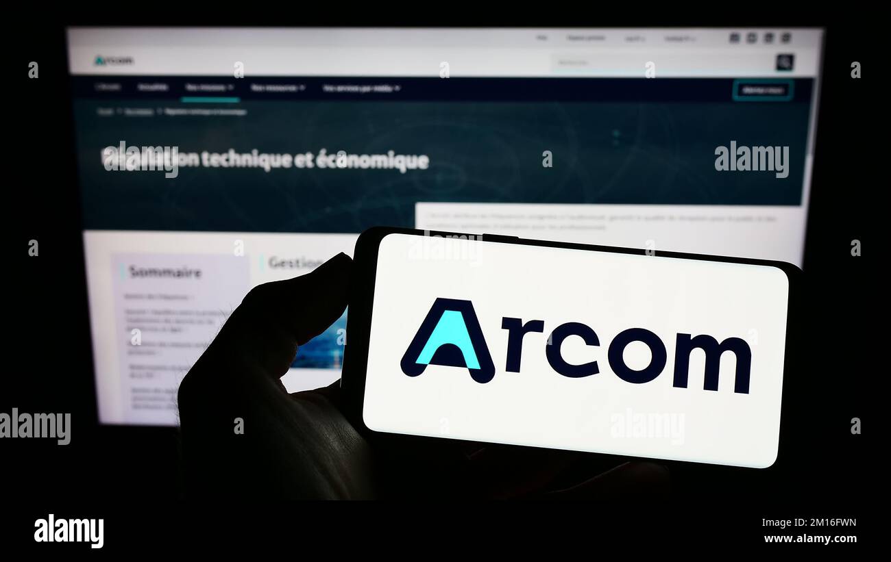 Person holding cellphone with logo of French digital regulation agency ARCOM on screen in front of webpage. Focus on phone display. Stock Photo