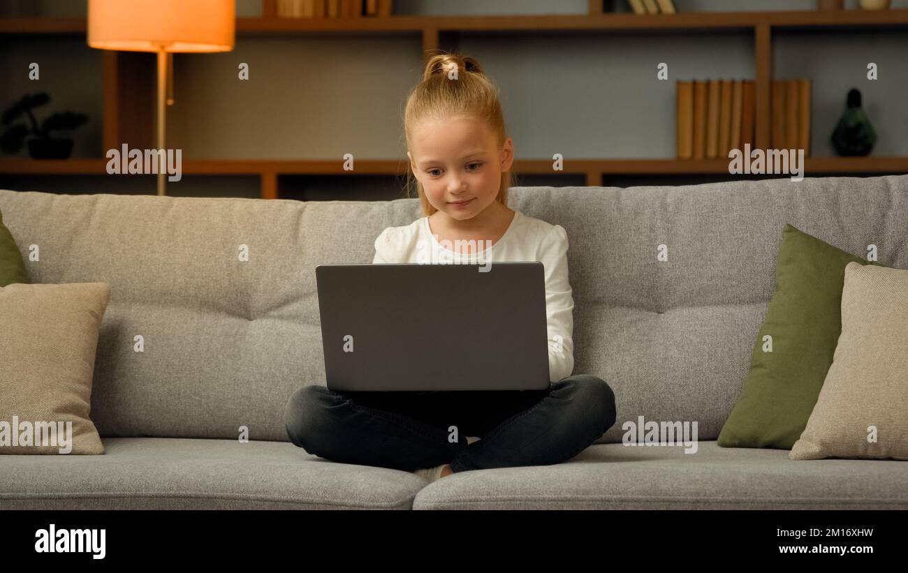 Cute little gamer schoolgirl child playing online modern computer games completing gaming level chatting message in social networks on laptop searchin Stock Photo