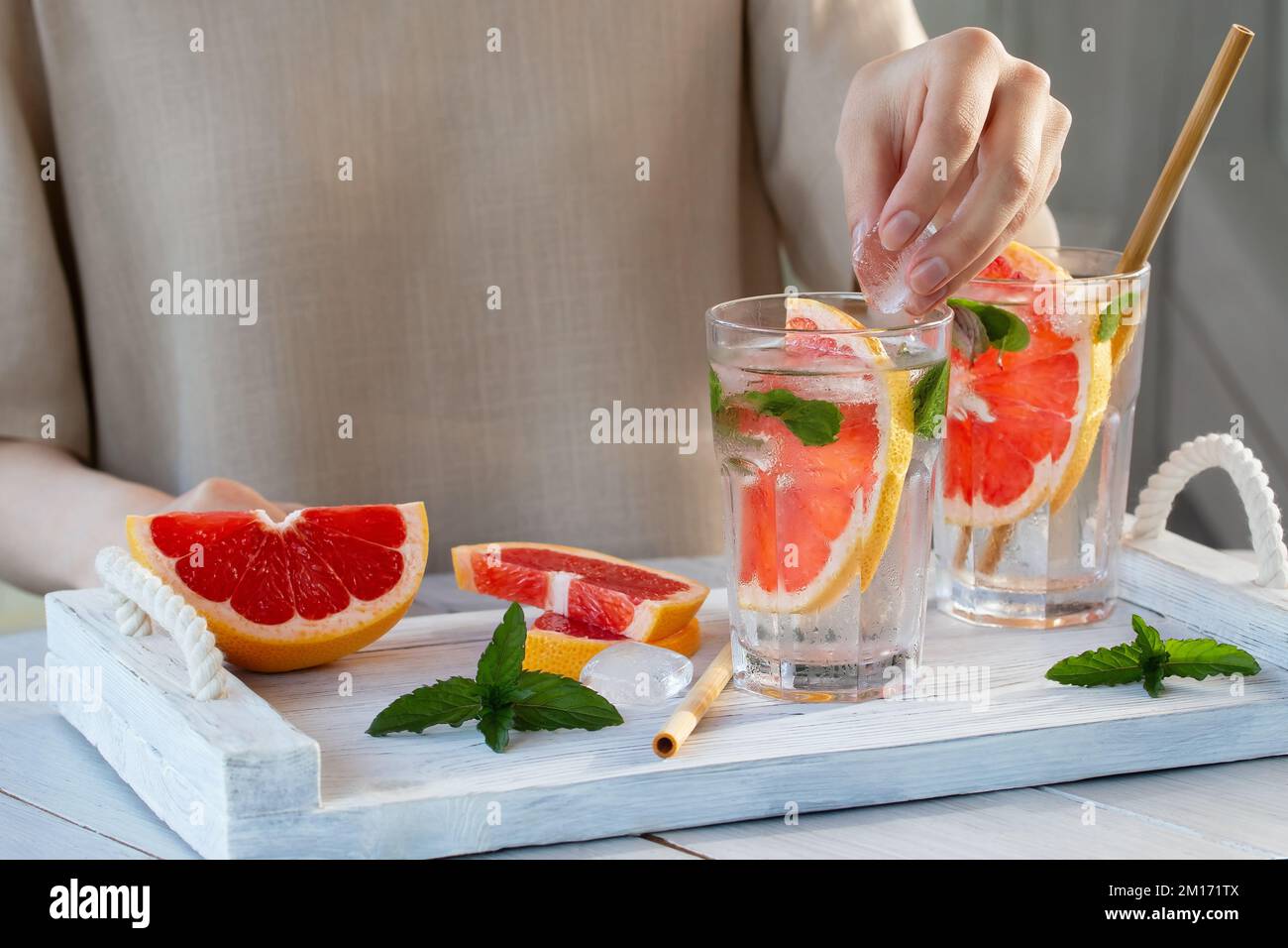Girl cooking summer refreshing fruit cocktail with grapefruit slices and mint. Stock Photo