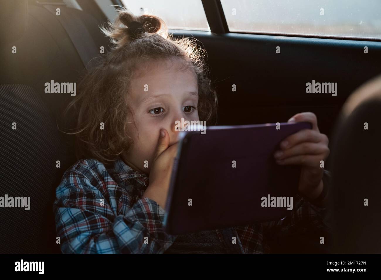 Screaming boy watching movie on computer tablet in car. Child using technology.  Stock Photo