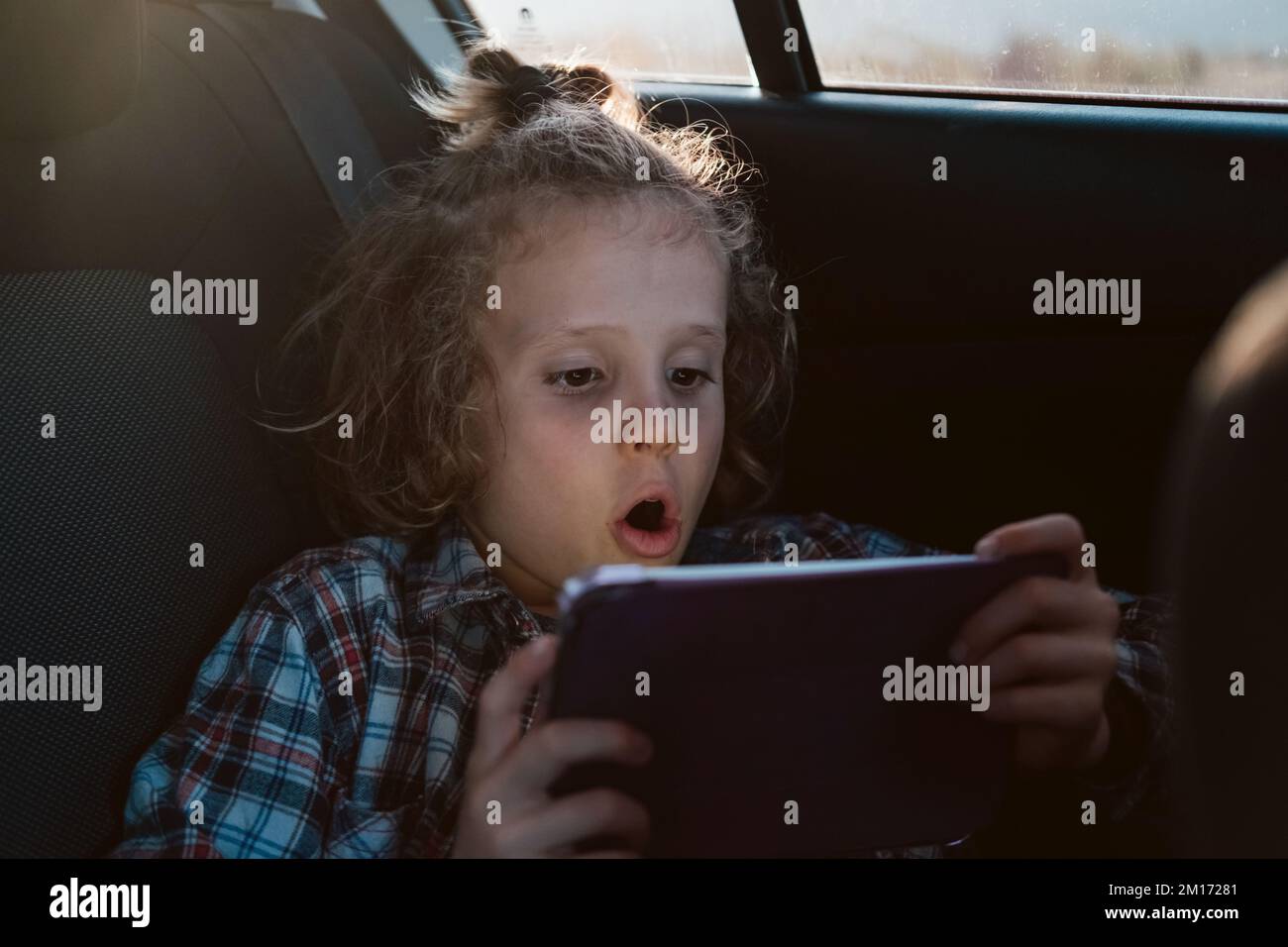 Excited boy watching a movie on technology tablet in car. Child using computer. Stock Photo