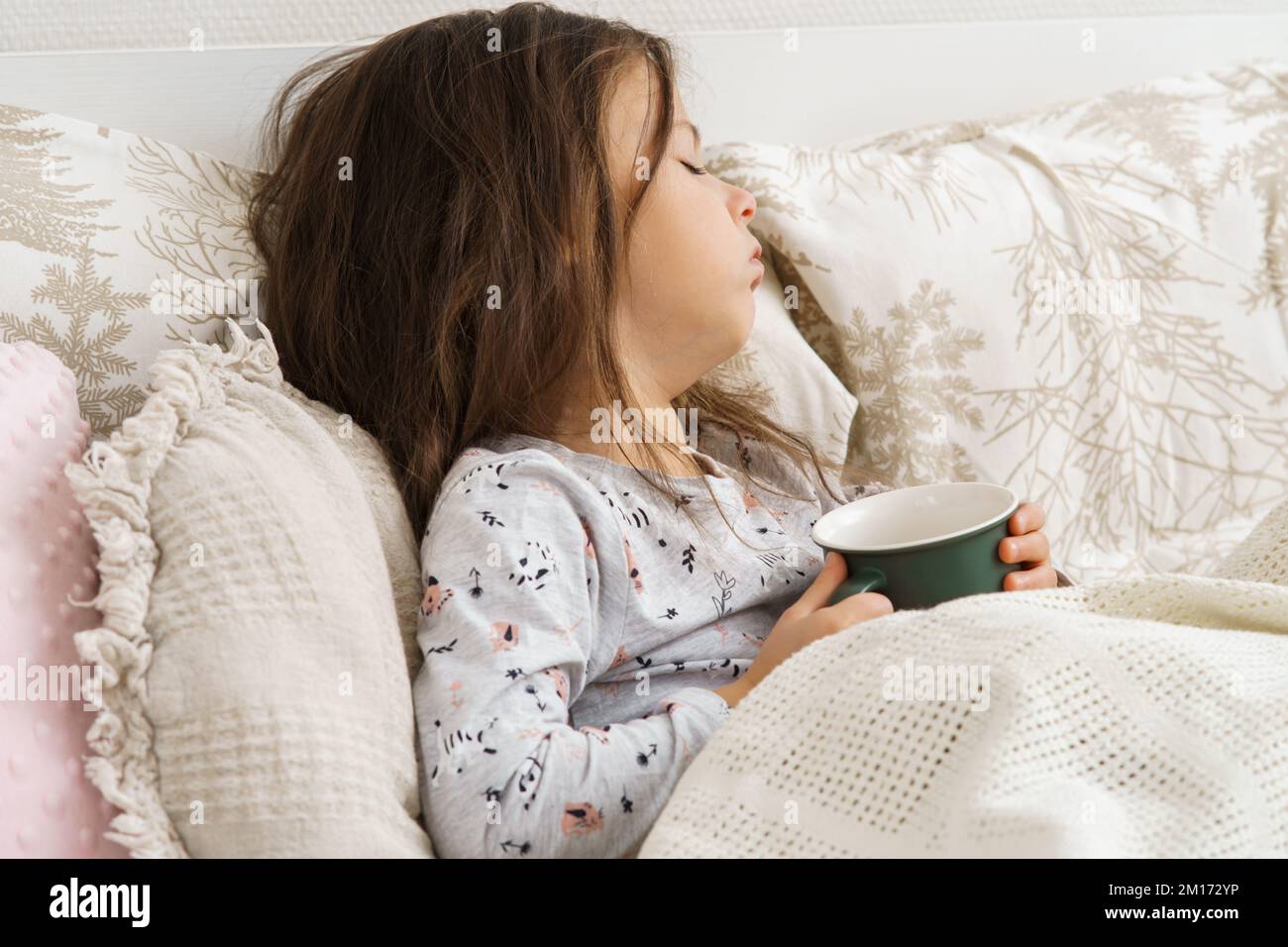 Dear little dark haired preschooler girl coughing, drinking hot tea or