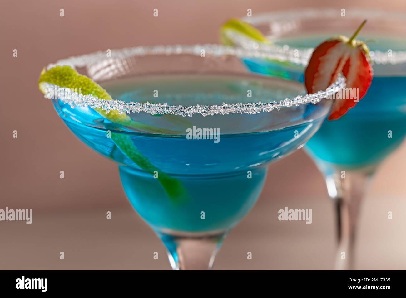 https://c8.alamy.com/comp/2M17335/two-glasses-with-blue-margarita-cocktail-garnished-with-lime-zest-and-strawberries-selective-focus-2M17335.jpg