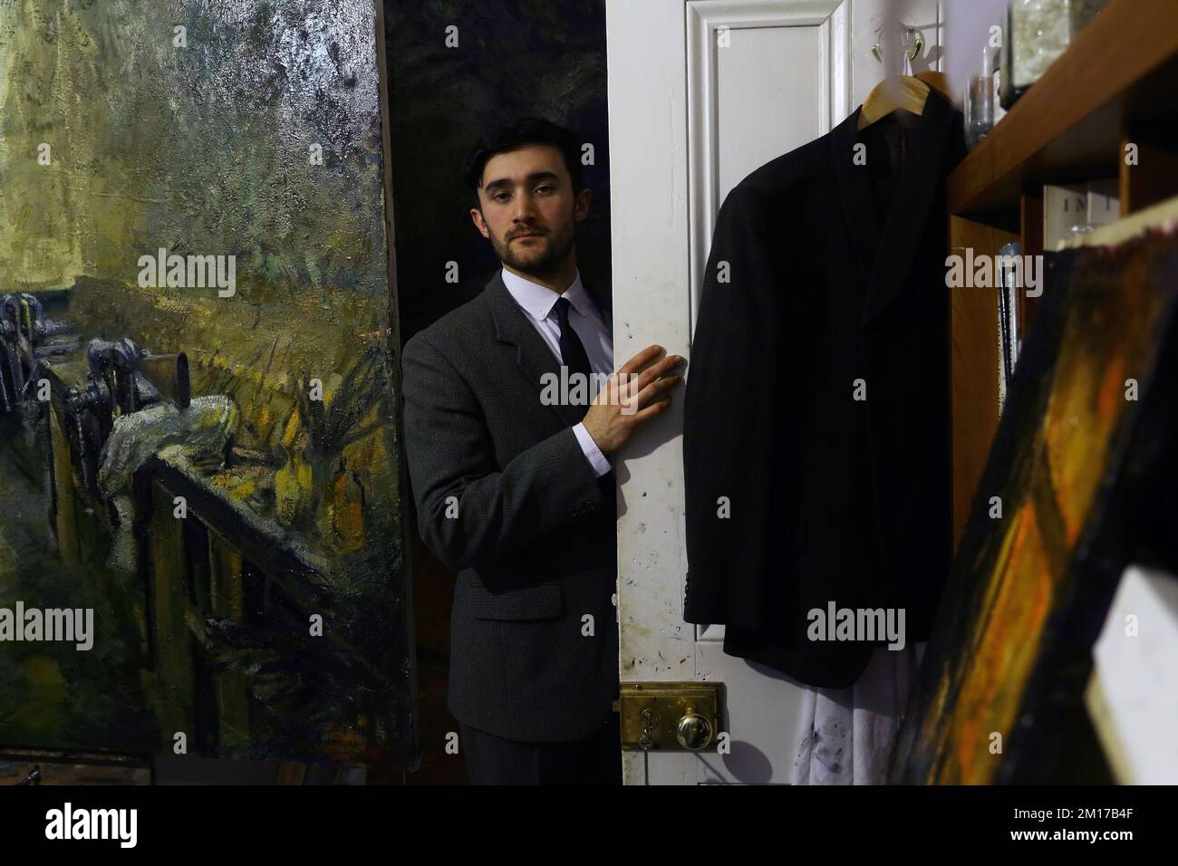 Elegant man dressed in suit opening door of artist studio with oil painting in background. Stock Photo