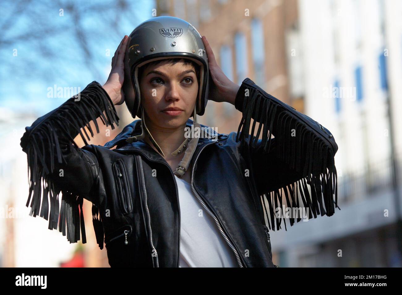 Beautiful female biker wearing a tasseled leather jacket and classic helmet Stock Photo