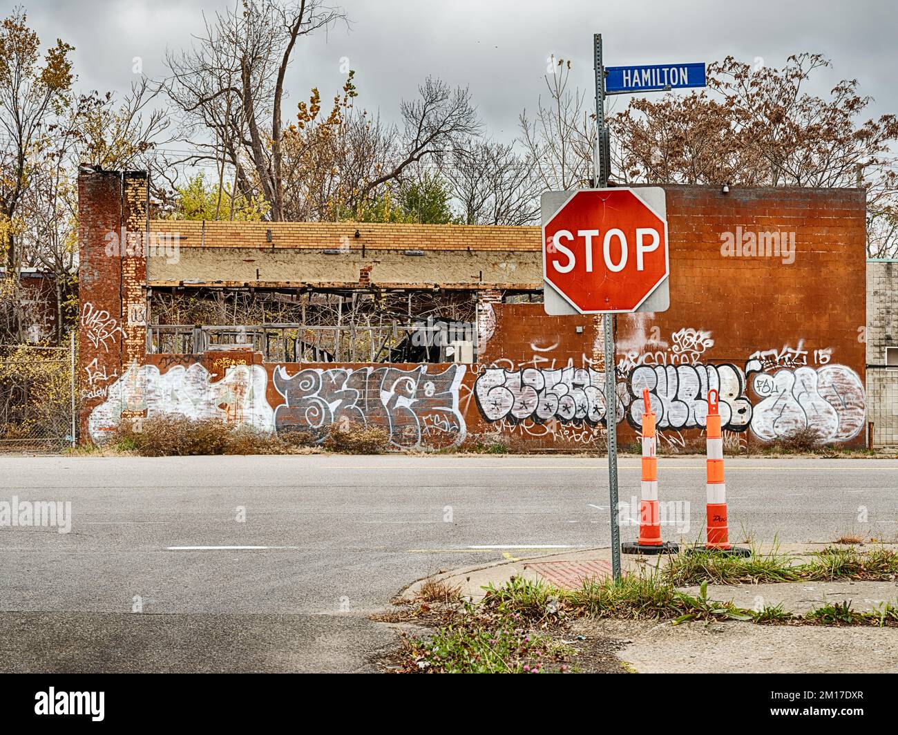 DETROIT, MICHIGAN - NOVEMBER 13, 2021: A stop sign on Hamilton Avenue stands in front of an abandoned business covered with graffiti in Detroit, Michi Stock Photo