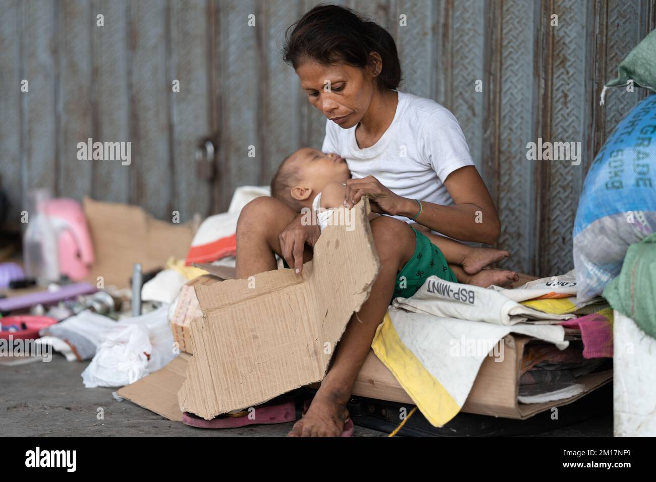 A homeless woman sits with her child on a makeshift bed made of cardboard. Cebu City, Philippines Stock Photo