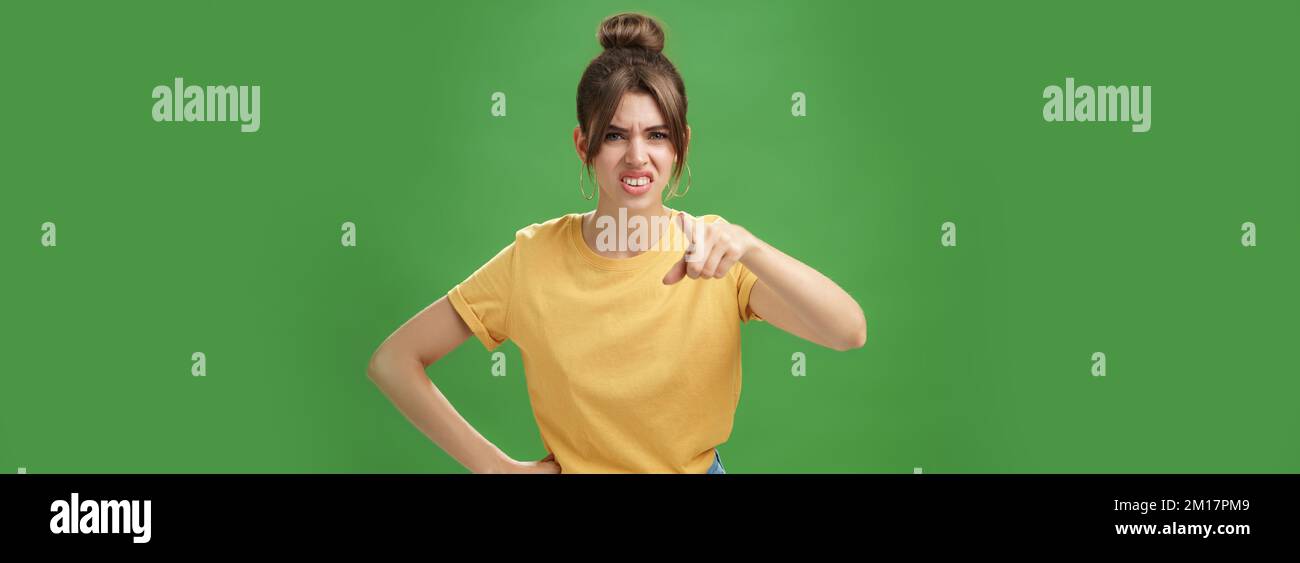 Portrait of arrogant impolite young woman in yellow t-shirt pointing at camera squinting and grimacing from disdain and scorn standing unimpressed Stock Photo