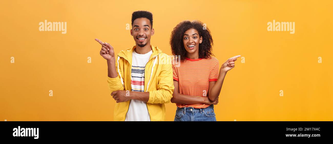 Which one telling true. Joyful and friendly good-looking couple, african american woman pointing left and dark-skinned guy right smiling broadly at Stock Photo