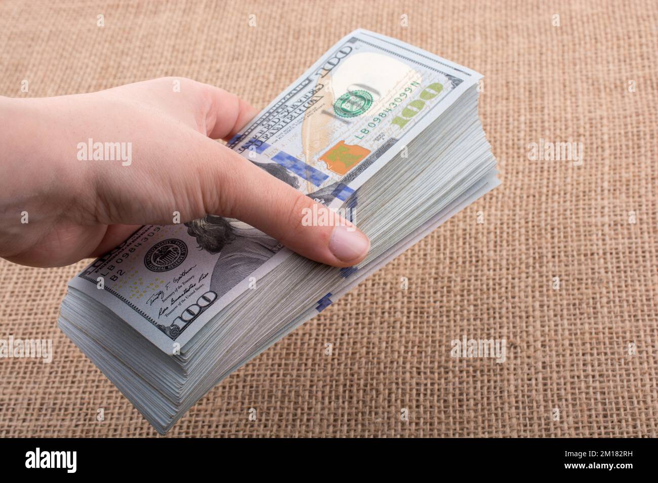 Hand holding banknote bundle of US dollar on a linen canvas background ...