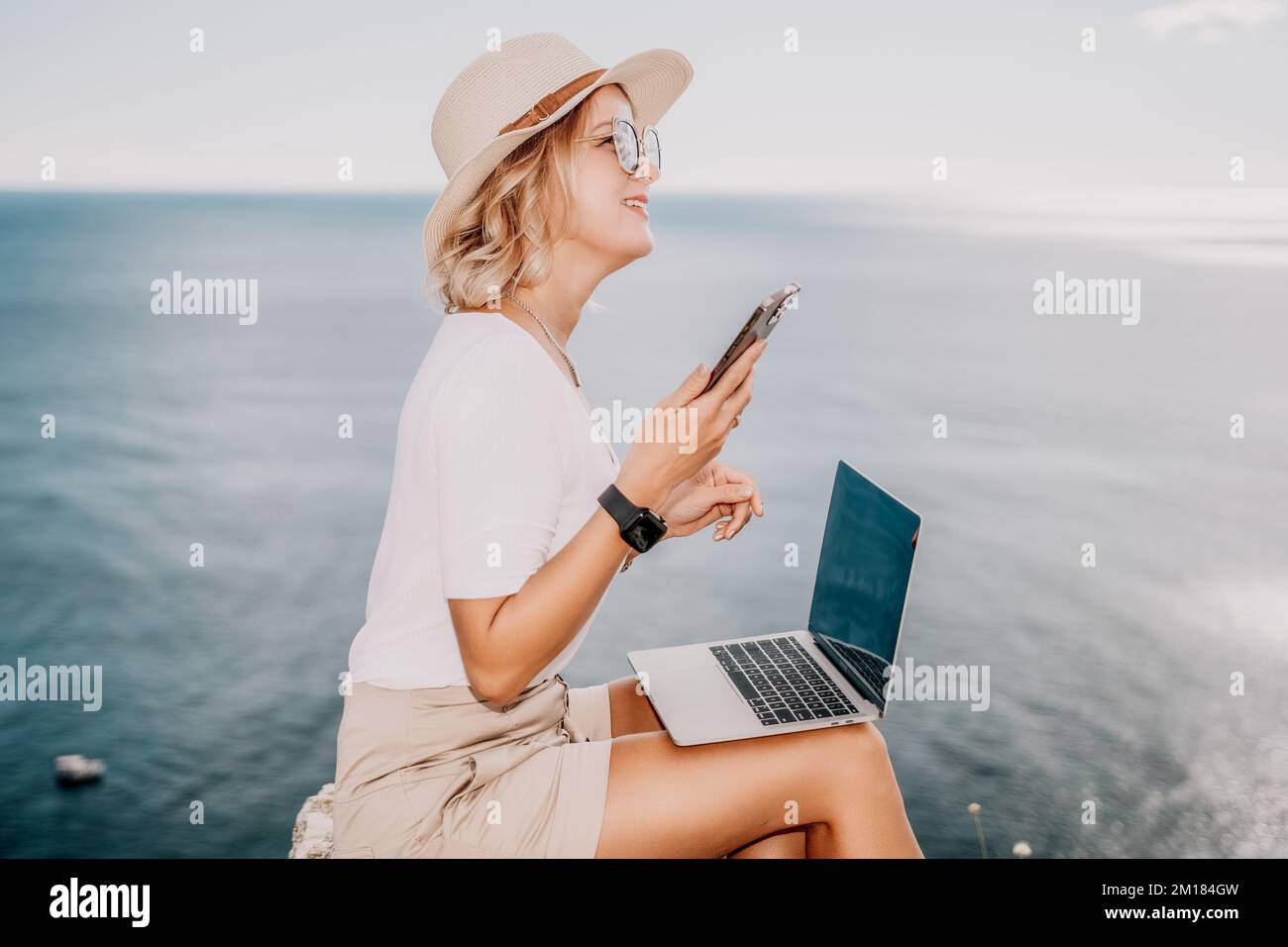 Digital nomad, Business woman working on laptop by the sea. Pretty lady typing on computer by the sea at sunset, makes a business transaction online Stock Photo