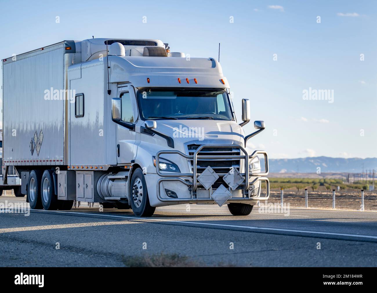 Industrial comfortable big rig white semi truck tractor with extended cab transporting frozen commercial cargo in refrigerator semi trailer running on Stock Photo