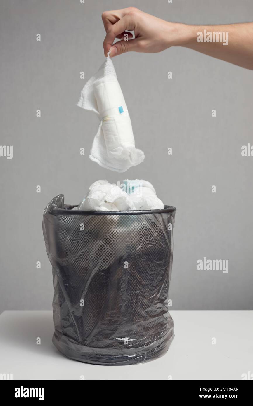 Person throws used diapers into loaded bin against grey wall Stock