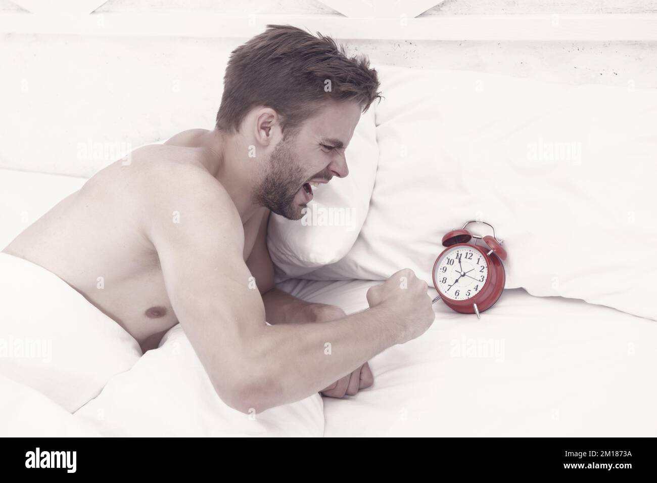 He is late. Angry guy break alarm clock in bed. Unshaven man awake from sleep. Keeping late hours. Wake timer. Wakeup time. Morning stress. Being late Stock Photo