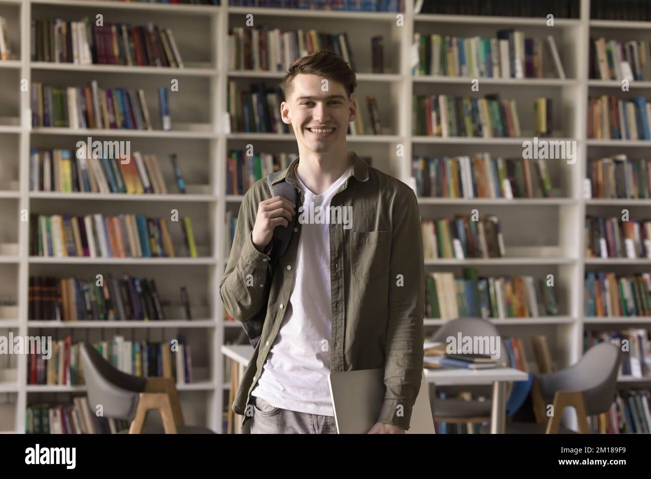 Happy handsome teenage student guy with backpack standing in library Stock Photo