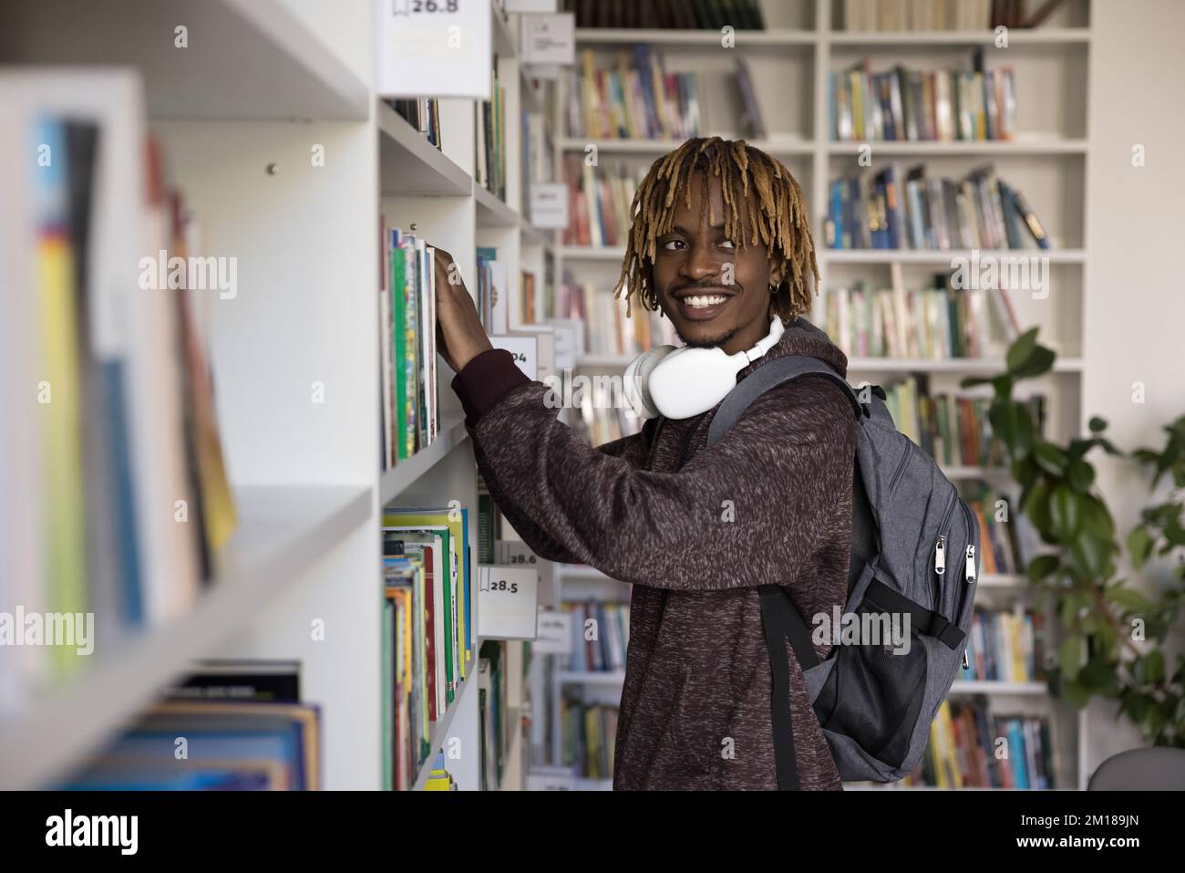 Cheerful satisfied Black student guy choosing textbook on shelf Stock Photo