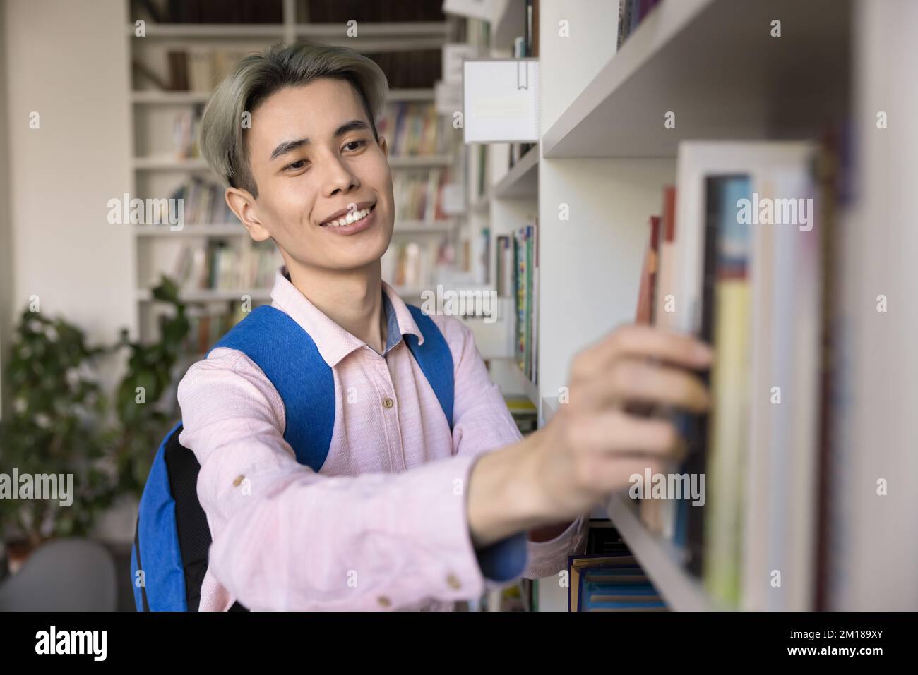 Happy Asian teen student guy choosing literature in university library Stock Photo