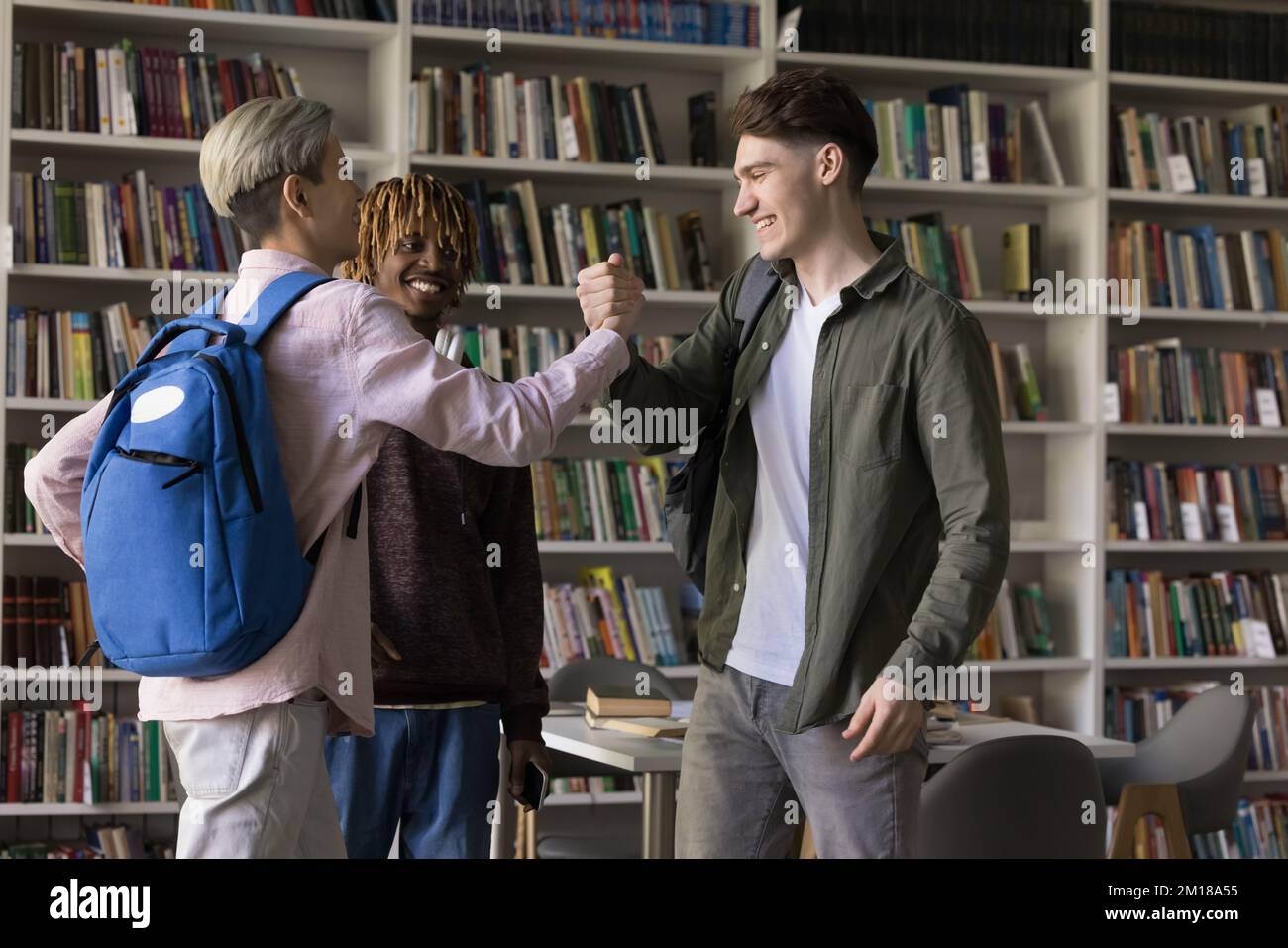 Cheerful young student guys meeting in university library for studying Stock Photo