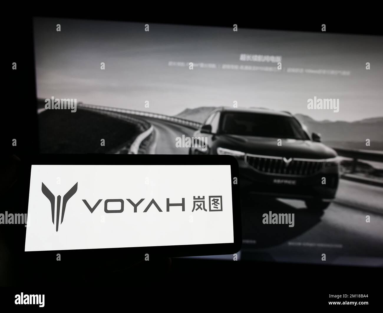 Person holding smartphone with logo of Chinese luxury car manufacturer Voyah on screen in front of website. Focus on phone display. Stock Photo