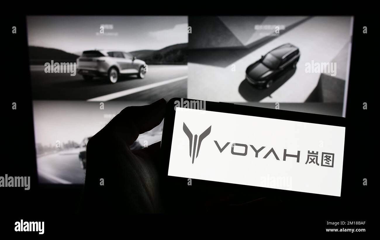 Person holding cellphone with logo of Chinese luxury car manufacturer Voyah on screen in front of business webpage. Focus on phone display. Stock Photo