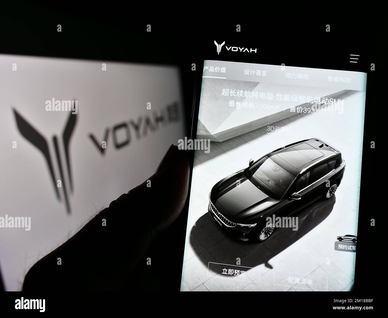Person holding cellphone with website of Chinese luxury car manufacturer Voyah on screen in front of logo. Focus on center of phone display. Stock Photo