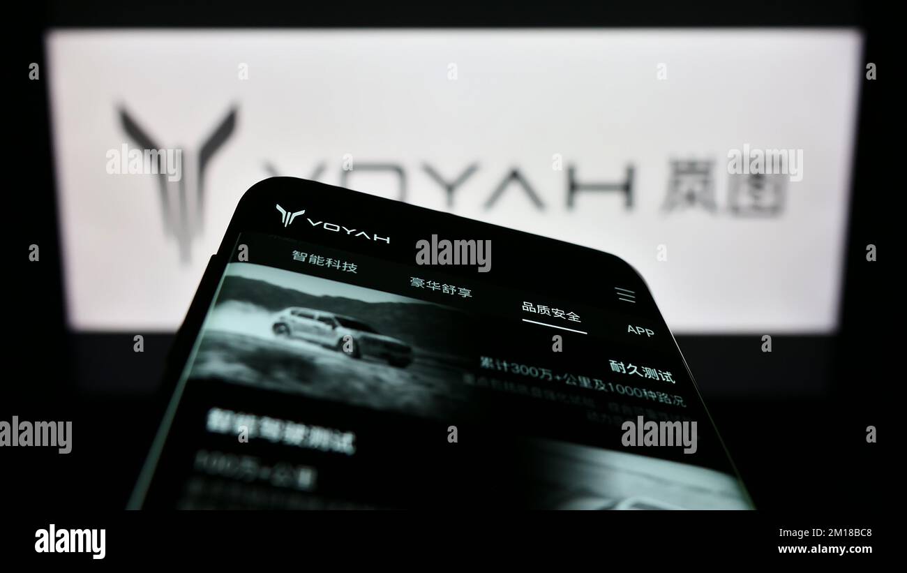 Mobile phone with webpage of Chinese luxury car manufacturer Voyah on screen in front of company logo. Focus on top-left of phone display. Stock Photo