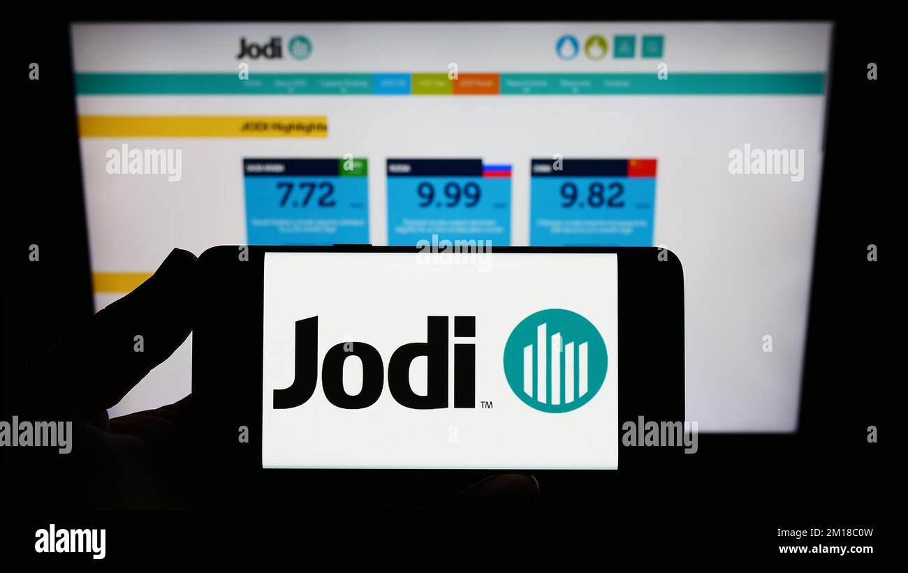 Person holding smartphone with logo of Joint Organisations Data Initiative (JODI) on screen in front of website. Focus on phone display. Stock Photo
