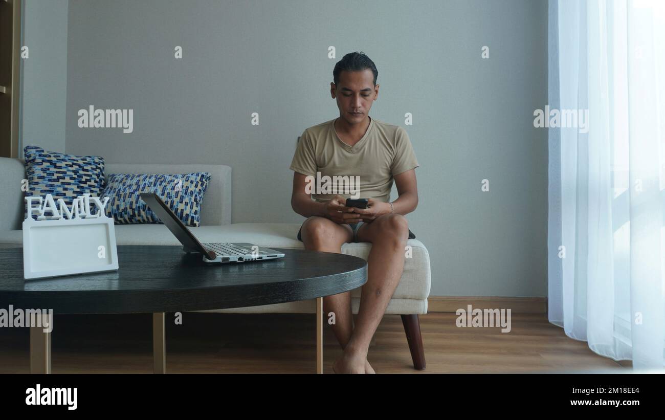 Man is using smartphone and laptop or notebook while working in the living room of the house Stock Photo